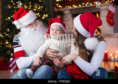 Famille heureuse avec son enfant ayant un amusement près de l'arbre de Noël et foyer au salon Banque D'Images