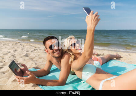 Couple heureux avec les gadgets modernes lying on beach Banque D'Images