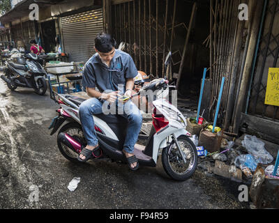 Bangkok, Bangkok, Thaïlande. 14 Décembre, 2015. Un homme est assis sur son scooter et vérifie son smart phone dans Bang Chak marché. Un grand nombre de boutiques dans le marché sont déjà fermées. Le marché se ferme de façon définitive le 31 décembre 2015. Le bang Chak Market sert la communauté autour de Di 91-97 sur Sukhumvit Road, dans la banlieue de Bangkok. Environ la moitié du marché a été démoli. Les autorités de la ville de Bangkok mis un avis à la fin de novembre que le marché serait fermé par le 1 er janvier 2016 et le réaménagement allait commencer peu après. Les vendeurs de marché dit condominiums sont construites sur la terre. (Credi Banque D'Images