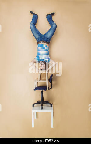 Homme debout sur un tas de chaises à l'envers. Studio shot sur fond beige. Banque D'Images