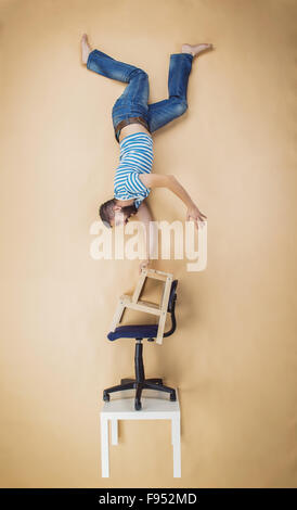 Homme debout sur un tas de chaises à l'envers. Studio shot sur un fond beige. Banque D'Images