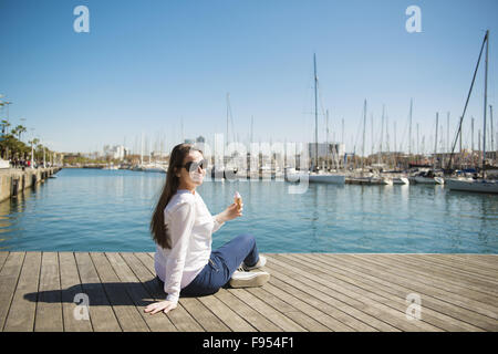 Happy young woman with ice cream est sitting on pier Banque D'Images