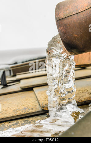 Eau gelée dans la gouttière, sur le toit enneigé, mountain house dans l'hiver froid . Banque D'Images