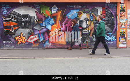 Jeune homme et femme marche passé certains street art sur volets dans Stevenson Square, Rue du levier, le centre-ville de Manchester, au Royaume-Uni. Banque D'Images