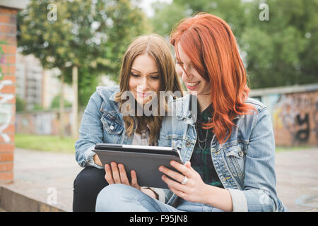 La moitié de la longueur de deux jeunes handsome young Blonde Redhead et les cheveux droits femmes assis sur un escalier à l'aide de tablette, à la Banque D'Images