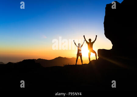 Couple d'équipe les randonneurs succès dans le coucher du soleil des montagnes, accomplir avec les bras tendus. Jeune homme et femme sur rocky mountain Banque D'Images