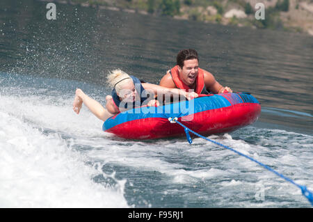 Brett et Kali rire comme ils tenir solidement sur le tube car il est tiré de l'arrière du bateau, sur le lac Kalamalka, C.-B. Banque D'Images