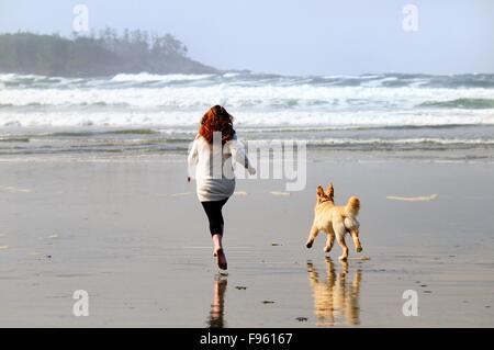 Une jeune femme et son chien (Golden Retriever) courir après un ballon sur Chesterman Beach près de Tofino, en Colombie-Britannique. Banque D'Images