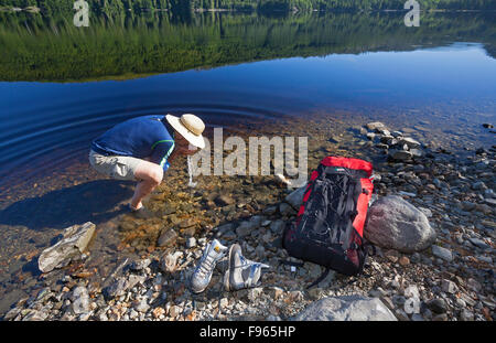Un randonneur prenant une pause fraîcheur des boissons dans les eaux claires de Nawhitti lac situé le long de la route de Holberg Banque D'Images