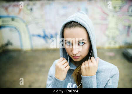 Adolescente grave avec le capot sur l'écoute de la musique à partir d'écouteurs debout sur fond de mur de graffiti Banque D'Images