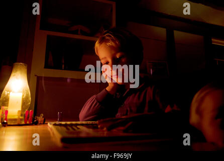 Un garçon se lit par la lumière de bougie juste avant le coucher. Banque D'Images