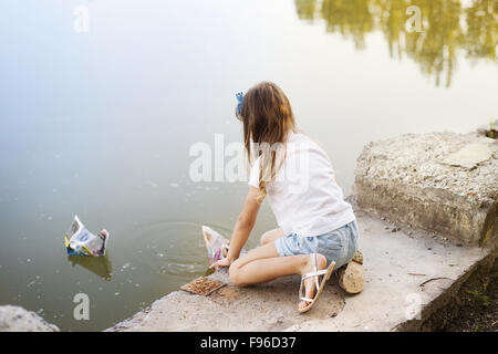 Petite fille jouant avec des bateaux en papier dans la rivière Banque D'Images