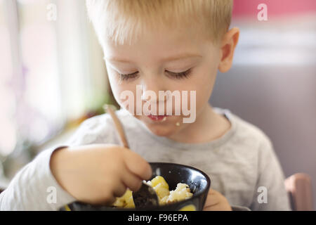 Adorable petit garçon blond de manger les pâtes de bol noir Banque D'Images