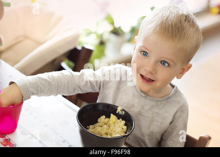 Adorable petit garçon blond de manger les pâtes de bol noir Banque D'Images