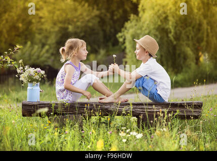 Cute boy and girl dans l'amour. Ils assis sur un banc au coucher du soleil. Banque D'Images