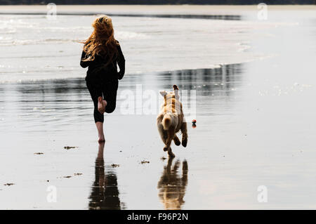 Une jeune femme et son Golden Retriever à courir après une balle pendant que sur Chesterman Beach à Tofino, en Colombie-Britannique. Banque D'Images