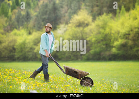 Jeune agriculteur pushing wheelbarrow dans le domaine Banque D'Images