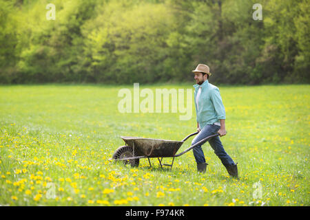 Jeune agriculteur pushing wheelbarrow dans le domaine Banque D'Images