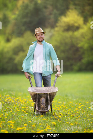 Jeune agriculteur pushing wheelbarrow dans le domaine Banque D'Images