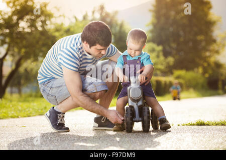 Jeune père avec son petit fils sur moto verte dans le parc ensoleillé Banque D'Images