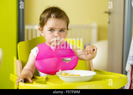 Petite fille dans une chaise haute est de manger un en-cas dans la cuisine Banque D'Images