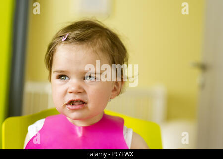 Petite fille dans une chaise haute est de manger un en-cas dans la cuisine Banque D'Images