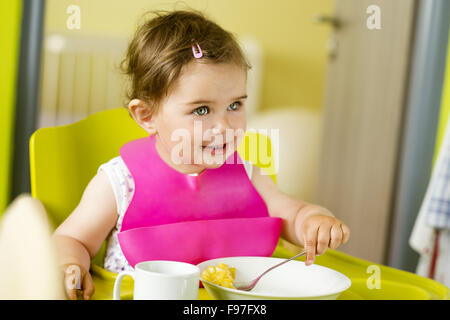 Petite fille dans une chaise haute est de manger un en-cas dans la cuisine Banque D'Images