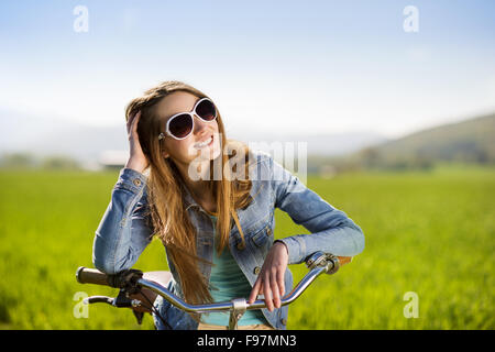 Jolie jeune fille avec vélo dans green field Banque D'Images