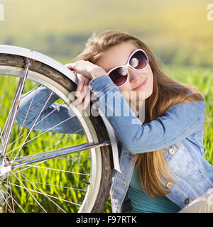 Jolie jeune fille avec vélo dans green field Banque D'Images