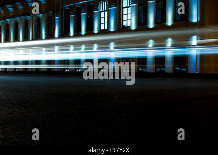 Voitures créer de la lumière bleu électrique light trails pendant qu'ils se déplacent au-delà d'un bâtiment éclairé au néon dans la nuit Banque D'Images