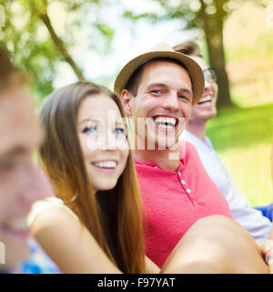 Groupe de jeunes gens s'amuser dans le parc, assis sur l'herbe Banque D'Images