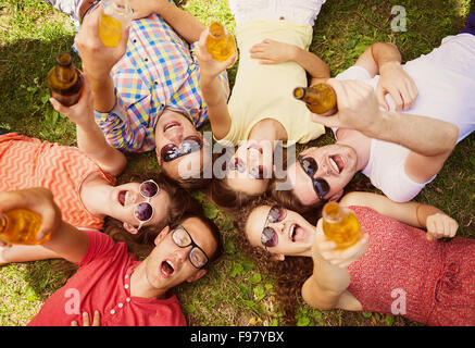 Groupe de jeunes gens s'amuser dans le parc, allongé sur l'herbe avec boissons Banque D'Images