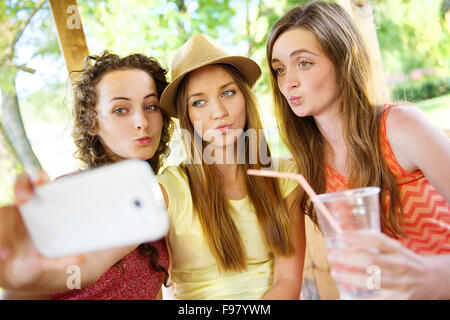 Trois belles filles boire et prendre avec selfies smartphone dans jardin pub Banque D'Images