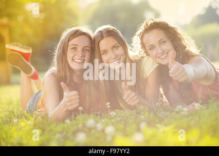Trois belles filles rient ensemble et couché sur l'herbe à l'extérieur dans un parc. Banque D'Images