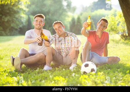 Trois professionnels amis passer du temps libre ensemble dans park sitting on grass, boire de la bière et le chat Banque D'Images