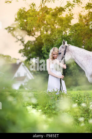 Femme en robe blanche balade à cheval dans la verte campagne Banque D'Images