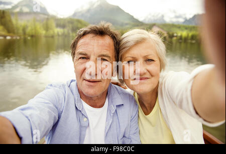 Couple sur un bateau avec montagnes en arrière-plan en tenant selfies Banque D'Images