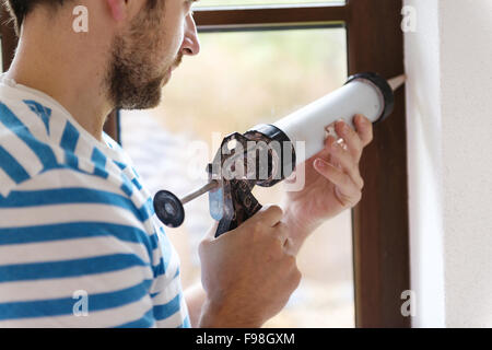L'homme d'appliquer un joint en silicone avec un pistolet à calfeutrer Banque D'Images
