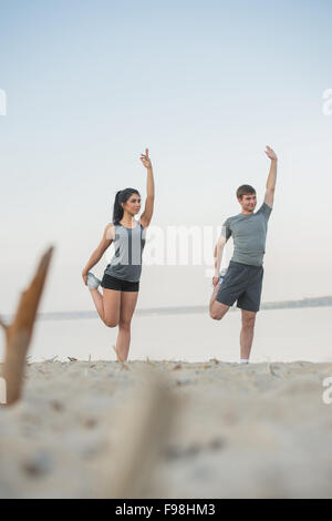 Jeune couple stretching on beach Banque D'Images