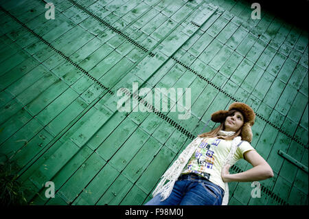 Jeune et belle en hiver hat posing en face de green woodden fence Banque D'Images