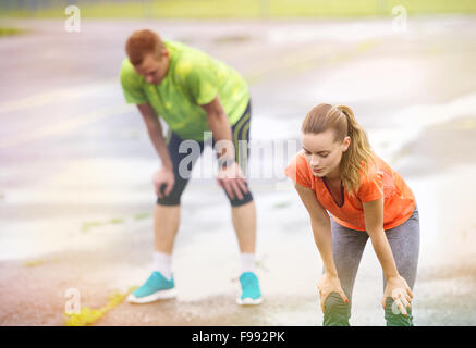 Jeune couple s'étendant à l'issue de la course sur l'asphalte par temps de pluie Banque D'Images