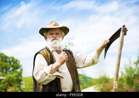 Vieux fermier avec scythe à prendre une pause pour tondre le gazon Banque D'Images