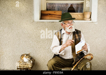 Vieil homme lisant le journal devant sa maison Banque D'Images