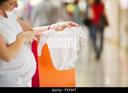 Jeune femme enceinte à la recherche de nouveaux vêtements pour bébé dans shopping mall Banque D'Images