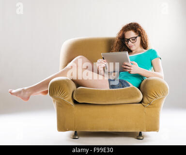 Beautiful Girl with digital tablet assis sur un fauteuil, isolé sur fond blanc Banque D'Images