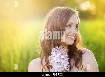 Belle femme avec des fleurs au printemps soleil. Girl est une holding lillac sur le pré vert. Banque D'Images