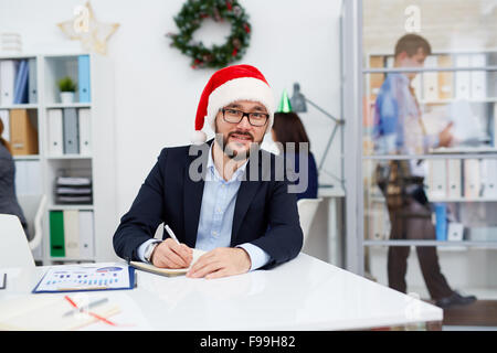 Santa heureux businessman looking at camera dans l'environnement de bureau Banque D'Images