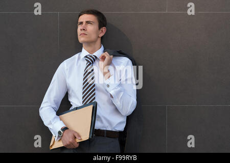 Perdu dans les pensées. Thoughtful businessman en soirée tenue de documents et à la recherche, tandis que l'article contre w gris Banque D'Images