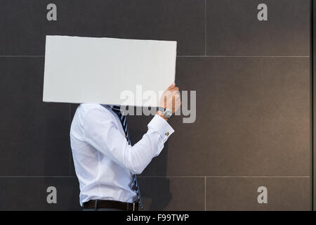 Portrait of smiling young woman showing blank signboard, avec copyspace salon pour le texte ou le slogan, contre mur gris b Banque D'Images