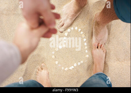 Pieds féminins et masculins de gros plan femme et l'homme se tenant la main et se tenait à côté de la coquille au coeur de la plage de sable Banque D'Images